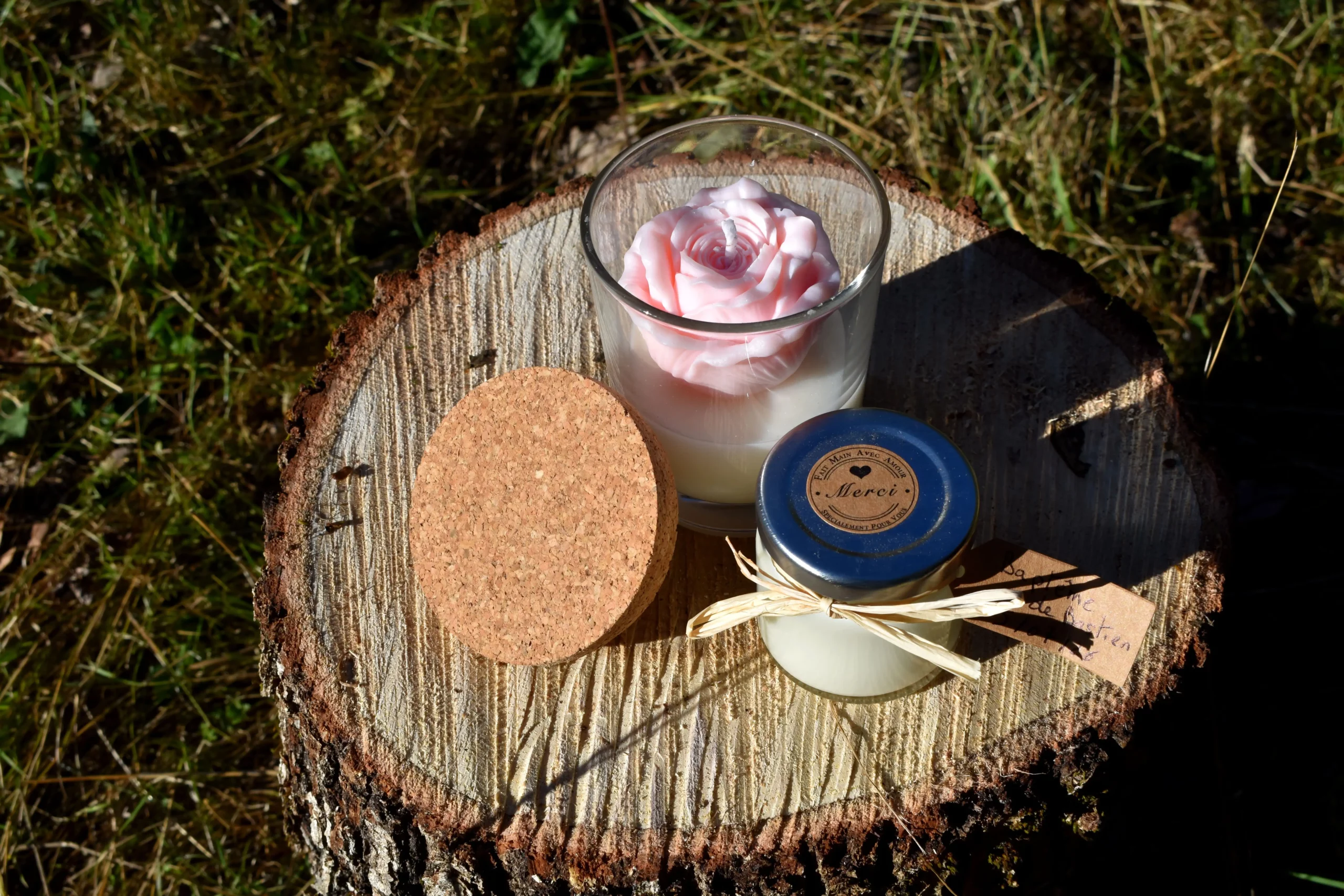 Bougies personnalisées, avec un petit format spécial baptême, une bougie moulé en forme de rose la fleur, tout ça posé sur une souche d'arbre dans un champs de montagne